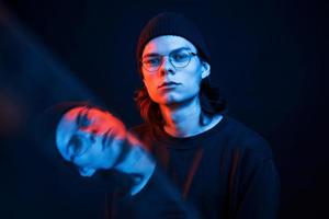 Face reflecting in the glass. Studio shot in dark studio with neon light. Portrait of serious man photo