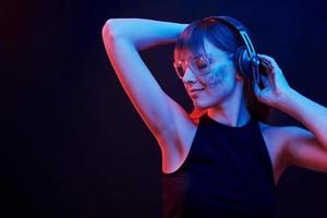 Touching headphones and listening to the music. Studio shot in dark studio with neon light. Portrait of young girl photo
