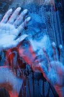 Looking with interest. Studio shot in dark studio with neon light. Portrait of beautiful girl behind wet glass photo