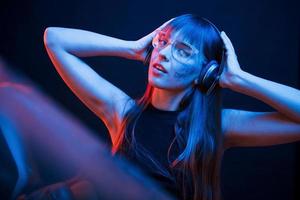 Quality music in headphones. Studio shot in dark studio with neon light. Portrait of young girl photo