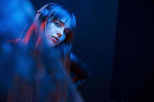 In black clothes. Studio shot in dark studio with neon light. Portrait of young girl photo