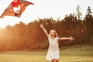 Amazing sunbeams. Happy girl in white clothes have fun with kite in the field. Beautiful nature photo