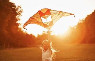 At sunset time. Happy girl in white clothes have fun with kite in the field. Beautiful nature photo