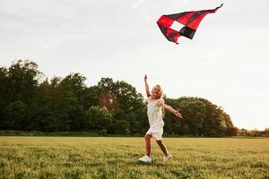 Come joing me. Happy girl in white clothes have fun with kite in the field. Beautiful nature photo