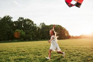 There is hot here, but wind is helping to refresh. Happy girl in white clothes have fun with kite in the field. Beautiful nature photo