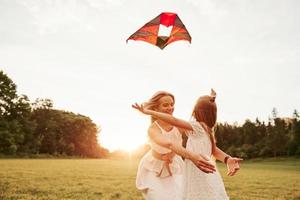 Embracing each other. Mother and daughter have fun with kite in the field. Beautiful nature photo