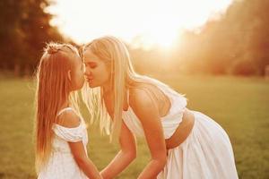 Kissing the child. Mother and daughter enjoying weekend together by walking outdoors in the field. Beautiful nature photo