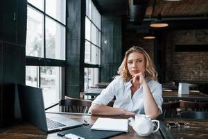 Portrait of confident girl. Businesswoman with curly blonde hair indoors in cafe at daytime photo