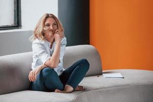 Full length photo. Businesswoman with curly blonde hair sitting in room against window photo