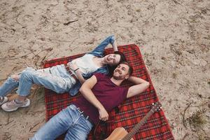 Top view. Young couple have picnic on the beach. Lying on the red colored blanket photo