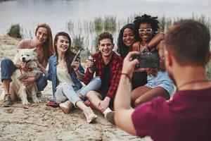 Te tomaré una foto en un segundo. grupo de personas hacen picnic en la playa. los amigos se divierten el fin de semana