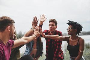 High five everyone. Group of people have picnic on the beach. Friends have fun at weekend time photo