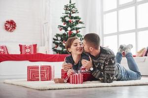 Conception of new year. Lovely young couple lying on the living room with green holiday tree at background photo