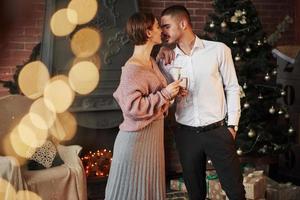 Emotional kiss. Nice couple celebrating new year in front of Christmas tree photo