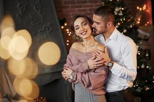 chico está tocando suavemente a su novia. linda pareja celebrando el año nuevo frente al árbol de navidad