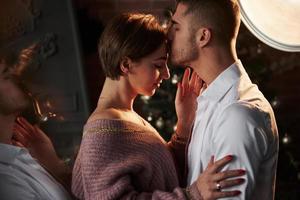 A kiss on the forehead. Closeness of the guy and girl in luxury wear that dancing and flirting. Gorgeous reflection from the side photo