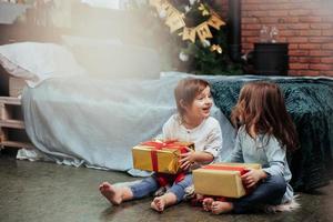 Cheerful mood. Christmas holidays with gifts for these two kids that sitting indoors in the nice room near the bed photo