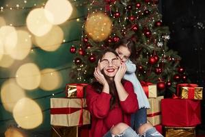buen gasto de tiempo en familia. linda niña que cubre los ojos de su madre. hermosa habitación con árbol de navidad y decoración navideña foto