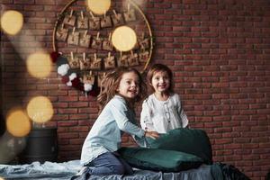 Young friends resting together. Little girls having fun on the bed with holiday interior at the background photo