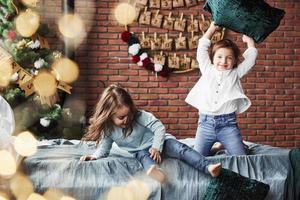 Looks like crazy pillow fight. Little girls having fun on the bed with holiday interior at the background photo