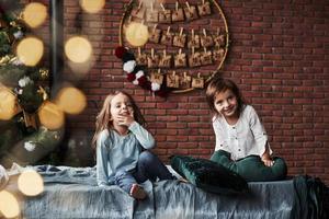 el árbol de navidad en el fondo crea un estado de ánimo de año nuevo. niñas divirtiéndose en la cama con interiores de vacaciones al fondo foto