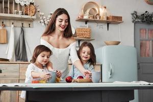 la chica va a probar el jugo nutricional. una mujer joven y hermosa les da bebidas a los niños mientras se sientan cerca de la mesa con juguetes foto