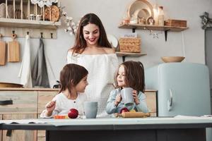 es delicioso, confía en mí. una mujer joven y hermosa les da bebidas a los niños mientras se sientan cerca de la mesa con juguetes foto