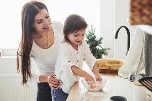 aprender a cocinar. feliz hija y mamá están preparando productos de panadería juntos. pequeño ayudante en la cocina foto