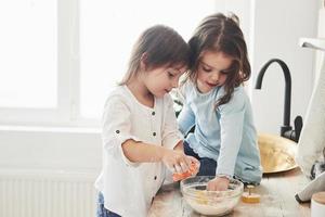 More like that they are playing. Preschool friends learning how to cook with flour in the white kitchen photo