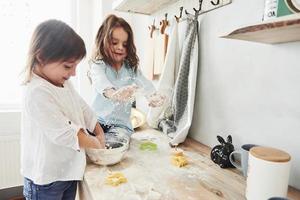 Funny kids are preparing the dough. Preschool friends learning how to cook with flour in the white kitchen photo