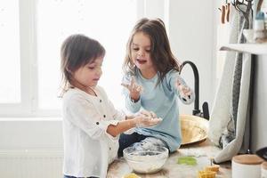 Children's games. Preschool friends learning how to cook with flour in the white kitchen photo