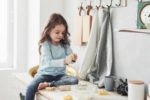 foto de una niña bonita que se sienta en la mesa de la cocina y juega con harina