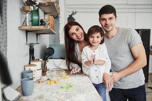 Near the table on the kitchen. Cute family posing for the picture photo