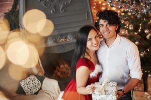 Gorgeous portrait. Beautiful couple celebrating New year in the decorated room with Christmas tree and fireplace behind photo