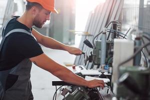 Operator of machine. Industrial worker indoors in factory. Young technician with orange hard hat photo