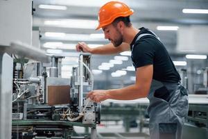 Operator of machine. Industrial worker indoors in factory. Young technician with orange hard hat photo