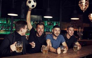 With soccer ball. It's a goal. Celebrating victory. Three sports fans in a bar watching football With beer in hands