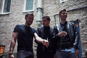 fumando juntos. tres amigos varones se encuentran fuera del bar. tener una conversación con ropa bonita foto