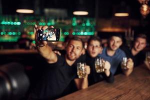 Making a selfie. Three friends resting in the pub with beer in hands. Having conversation photo