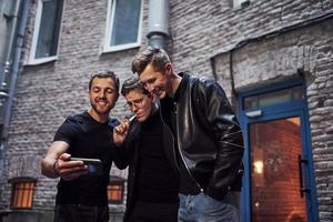 tres amigos varones se encuentran fuera del bar. tener una conversación con ropa bonita foto