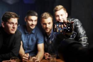 teléfono inteligente moderno. haciendo foto. amigos descansando en el pub con alcohol en las manos. teniendo una conversación