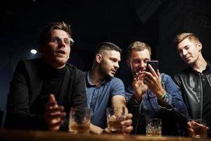 Front view. Friends resting in the pub with alcohol in hands. Having conversation photo