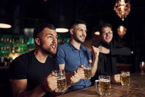 tres aficionados al deporte en un bar viendo fútbol. con cerveza en las manos foto