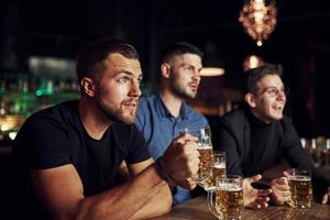 completamente concentrado. tres aficionados al deporte en un bar viendo fútbol. con cerveza en las manos