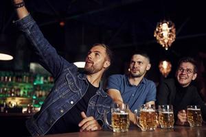 haciendo selfie tres aficionados al deporte en un bar viendo fútbol. con cerveza en las manos