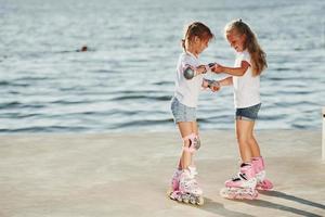 Two kids learning how to ride on roller skates at daytime near the lake photo