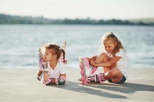 Two little girls with roller skates outdoors near the lake at background photo