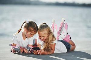 Lying down. Two little girls with roller skates outdoors near the lake at background photo