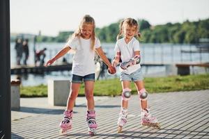 Two cute kids riding by roller skates in the park at daytime photo