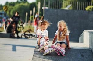 Having a rest. On the ramp for extreme sports. Two little girls with roller skates outdoors have fun photo